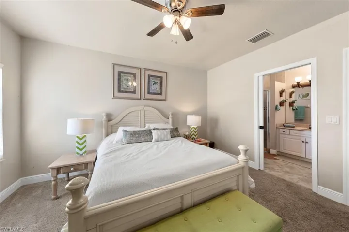 Bedroom featuring connected bathroom, baseboards, light colored carpet, and visible vents
