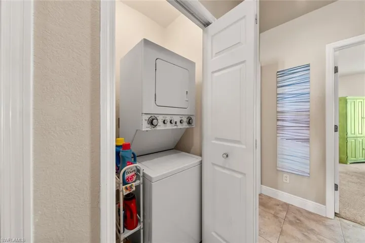 Laundry area featuring light tile patterned flooring, baseboards, stacked washer / dryer, and laundry area