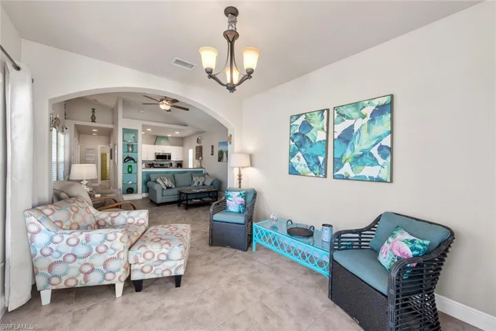 Living area featuring visible vents, baseboards, tile patterned floors, arched walkways, and ceiling fan with notable chandelier