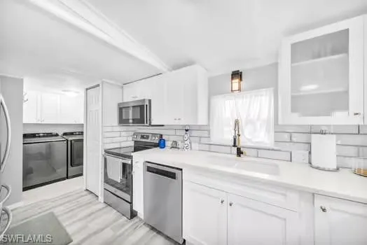 Kitchen with appliances with stainless steel finishes, white cabinetry, light countertops, washer and clothes dryer, and light wood-type flooring