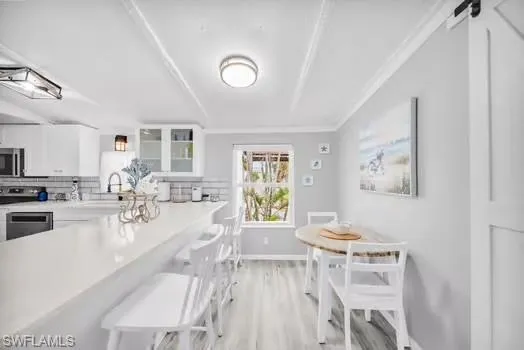 Kitchen featuring backsplash, a kitchen breakfast bar, white cabinets, light wood-type flooring, and crown molding
