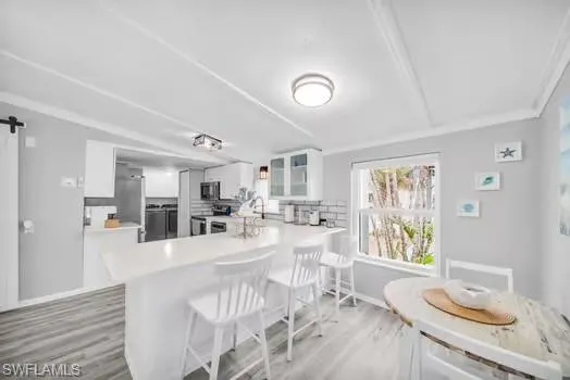 Kitchen with a barn door, white cabinetry, a kitchen bar, light countertops, and stainless steel appliances
