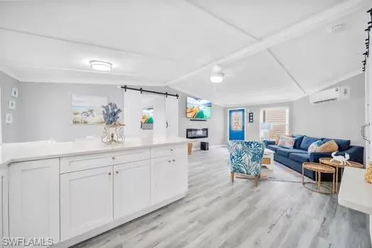 Living area with a barn door, vaulted ceiling, light wood-style flooring, and a wall mounted AC
