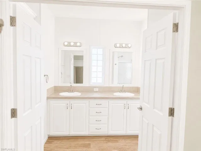 Bathroom with a dual vanity featuring white cabinetry, integrated sinks, light-toned countertop, and individual mirrors with vanity lighting