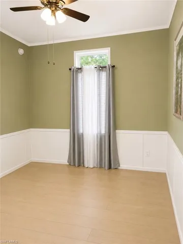 Room featuring wood-finish flooring, wainscoting, and a ceiling fan with integrated lighting