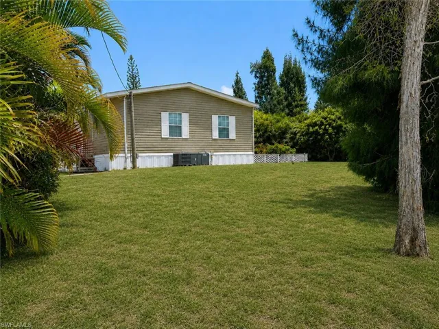 Expansive lawn area with mature trees and tropical foliage in the backyard