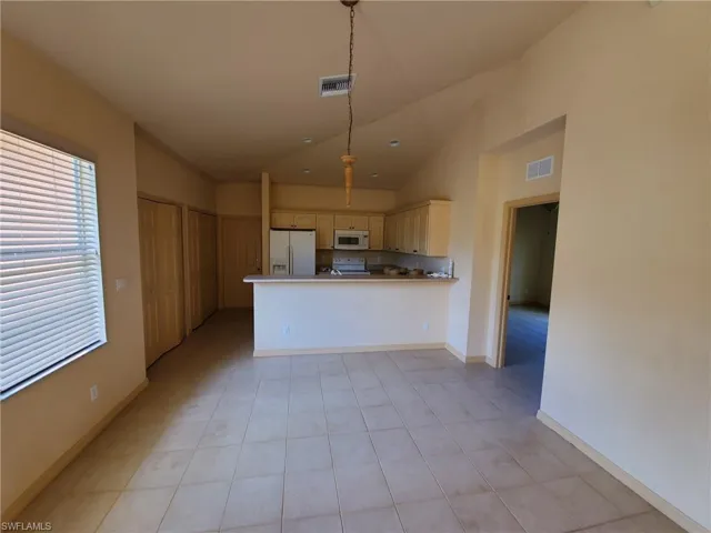 Kitchen featuring white appliances, kitchen peninsula, vaulted ceiling, and hanging light fixtures