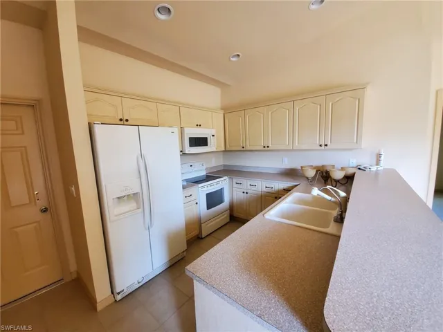 Kitchen with sink, kitchen peninsula, white appliances, light tile patterned floors, and cream cabinets
