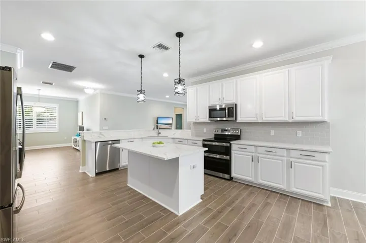 Kitchen featuring stainless steel appliances, white cabinets, a peninsula, pendant lighting, and ornamental molding