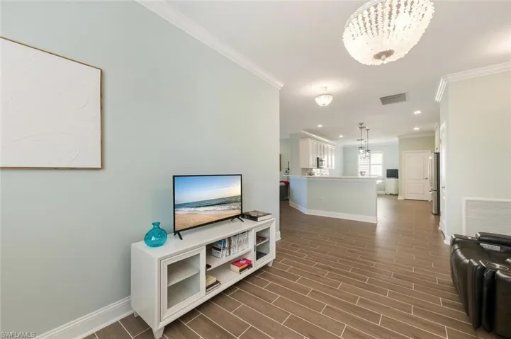 Living room with crown molding, wood tiled floors, and hanging lights
