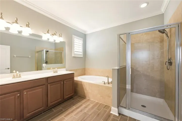 Bathroom featuring double vanity, ornamental molding, wood tiled floors, a garden tub, and a stall shower