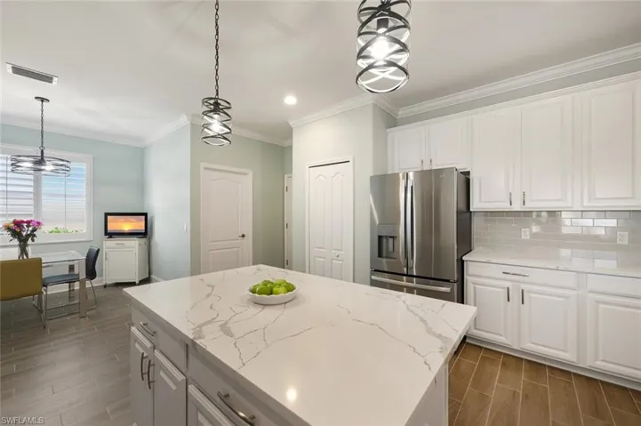 Kitchen with white cabinetry, stainless steel refrigerator with ice dispenser,  tile floors, and ornamental molding