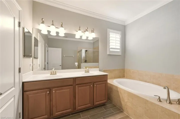 Full bathroom with double vanity, a garden tub, ornamental molding, and a stall shower