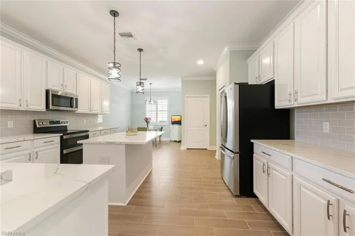 Featuring backsplash, stainless steel appliances, hanging light fixtures, white cabinetry, and ornamental molding