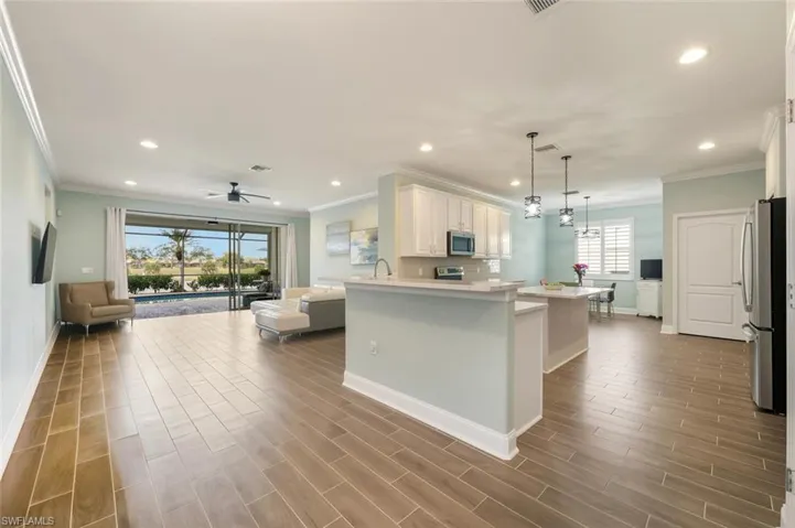Kitchen featuring open floor plan, white cabinetry, wood tiled floors, stainless steel appliances, and ornamental molding