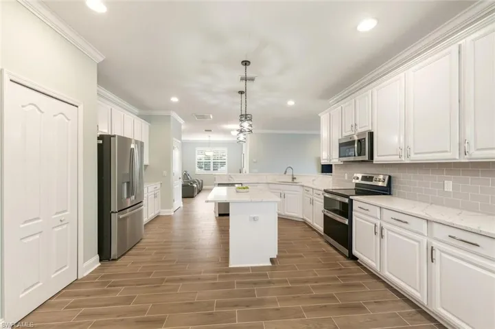 Kitchen featuring decorative light fixtures, white cabinets, stainless steel appliances, a peninsula, and crown molding