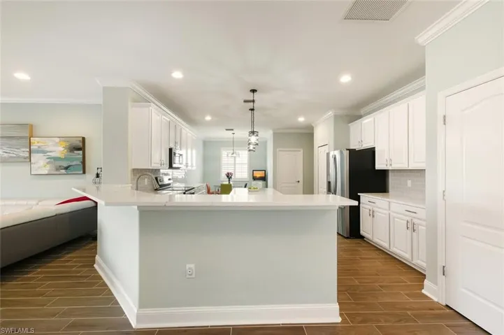 Kitchen with wood tiled floors, white cabinets, hanging light fixtures, and crown molding