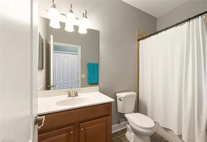 Full bath with vanity, a textured wall, and dark tile patterned flooring