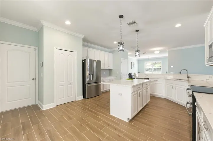 Kitchen featuring white cabinetry, stainless steel appliances, hanging light fixtures, a kitchen island, and wood tiled floors