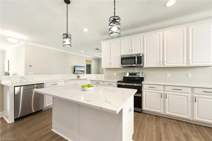 Kitchen featuring stainless steel appliances, ornamental molding, a peninsula, wood tiled floors, and pendant lighting