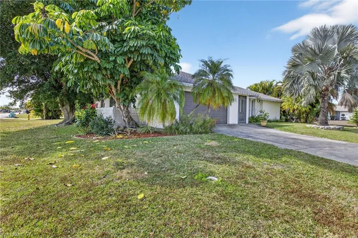 View of property hidden behind natural elements featuring concrete driveway, a front lawn, and an attached garage