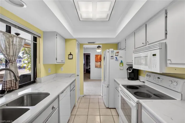 Kitchen with white appliances, white cabinets, a raised ceiling, light tile patterned floors, and light stone countertops