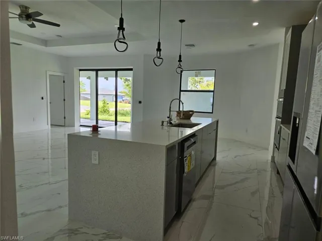 Kitchen with hanging light fixtures, an island with sink, sink, a wealth of natural light, and light tile patterned floors