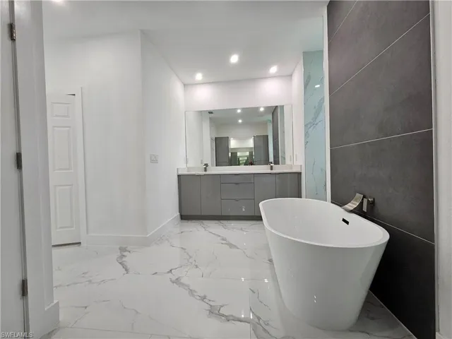 Bathroom with vanity, tile patterned flooring, tile walls, and a tub