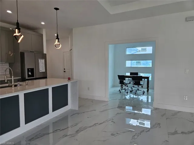 Kitchen featuring stainless steel fridge with ice dispenser, light tile patterned floors, backsplash, decorative light fixtures, and sink