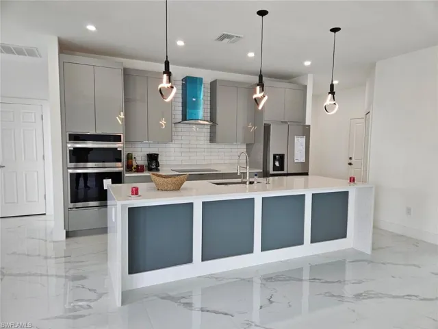 Kitchen with stainless steel appliances, sink, gray cabinets, decorative backsplash, and wall chimney exhaust hood