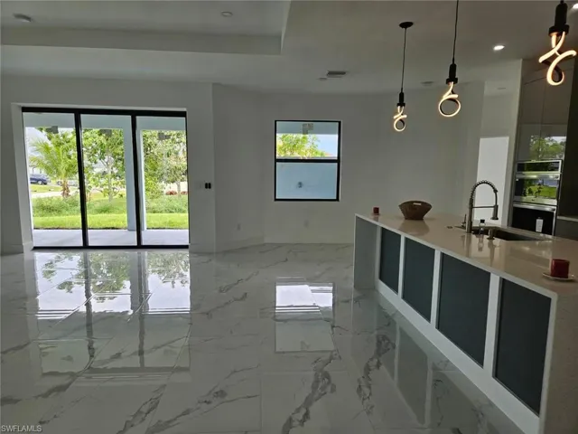Kitchen featuring light tile patterned floors, stainless steel double oven, sink, pendant lighting, and a center island with sink