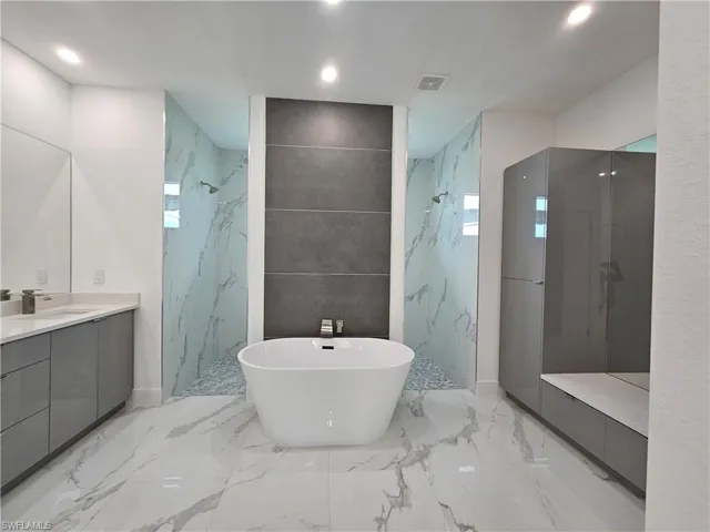 Bathroom with vanity, tile patterned flooring, tiled shower, and tile walls