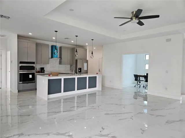 Kitchen with tasteful backsplash, stainless steel appliances, wall chimney exhaust hood, a center island with sink, and gray cabinetry