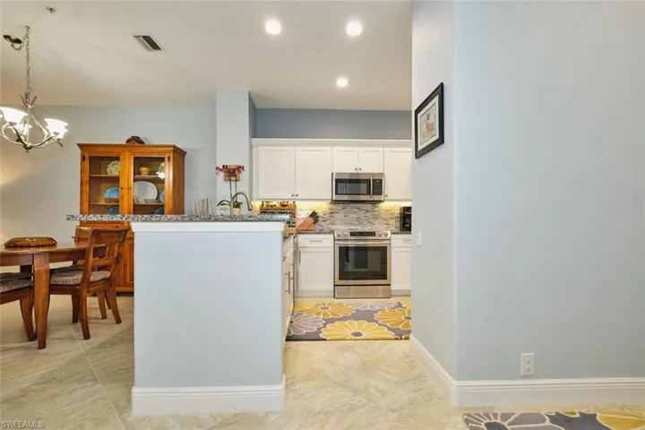 Kitchen featuring white cabinetry, stainless steel appliances, decorative backsplash, pendant lighting, and dark stone countertops