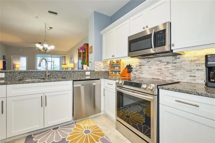 Kitchen with appliances with stainless steel finishes, white cabinets, a chandelier, and dark stone countertops