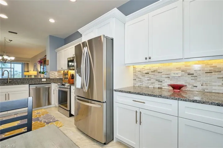 Kitchen with stainless steel appliances, white cabinetry, dark stone counters, hanging light fixtures, and a chandelier