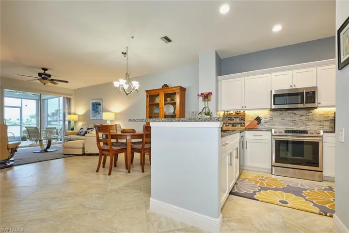 Kitchen with white cabinetry, appliances with stainless steel finishes, dark stone counters, hanging light fixtures, and a peninsula
