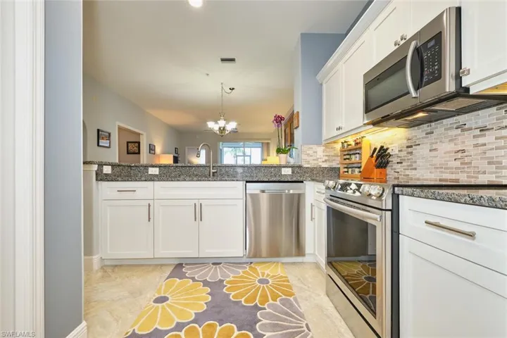 Kitchen featuring stainless steel appliances, a chandelier, white cabinets, decorative light fixtures, and dark stone countertops