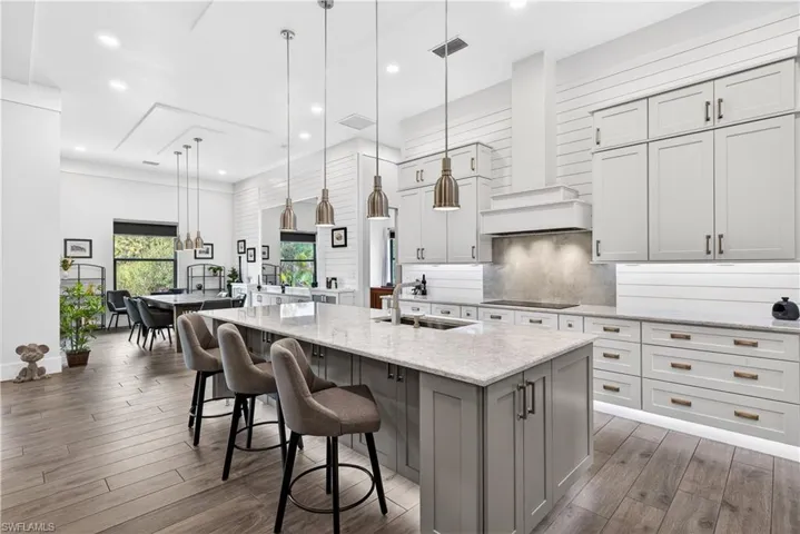Kitchen with hanging light fixtures, light stone counters, dark wood-type flooring, custom range hood, and tasteful backsplash