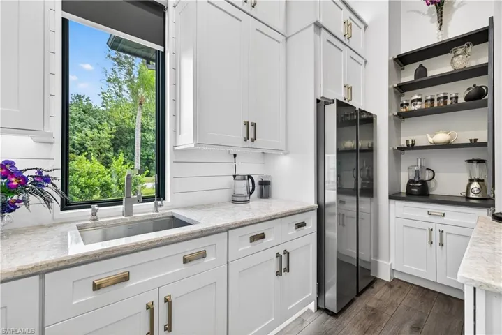 Kitchen featuring white cabinets, freestanding refrigerator, open shelves, light stone counters, and dark wood-style flooring