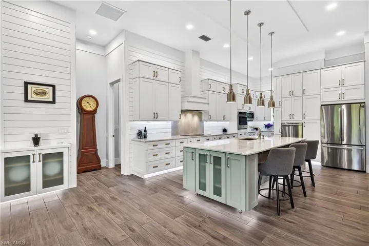 Kitchen with white cabinetry, appliances with stainless steel finishes, decorative light fixtures, a kitchen breakfast bar, and an island with sink
