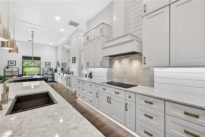 Kitchen with recessed lighting, light stone counters, premium range hood, white cabinetry, and decorative light fixtures