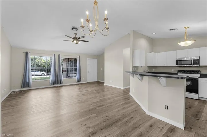 Kitchen featuring pendant lighting, white cabinets, ceiling fan with notable chandelier, electric stove, and a kitchen bar