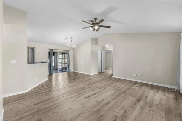 Unfurnished living room featuring ceiling fan with notable chandelier, light wood-type flooring, and lofted ceiling