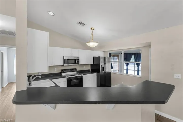 Kitchen with sink, white electric range oven, kitchen peninsula, black fridge with ice dispenser, and white cabinets