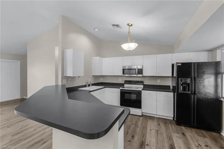 Kitchen featuring white cabinetry, kitchen peninsula, black fridge, and electric range