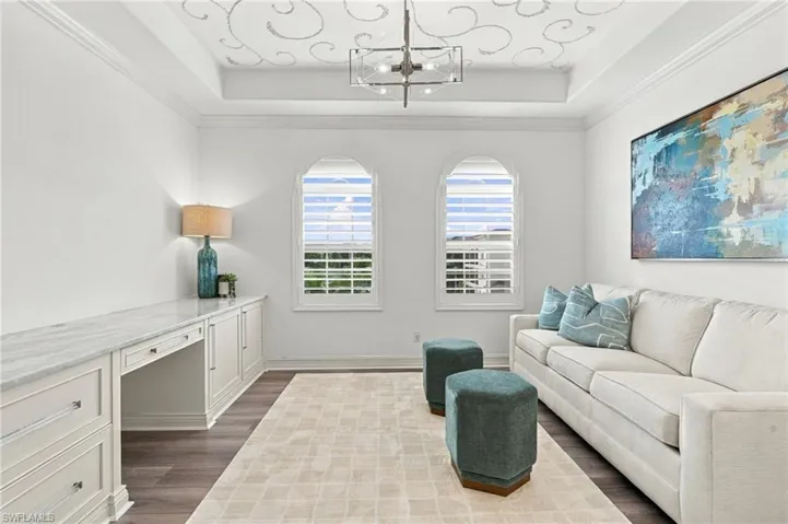 Tray ceiling with decorative detailing, arched windows featuring plantation shutters, built-in cabinetry with a stone countertop, and wood-finish flooring