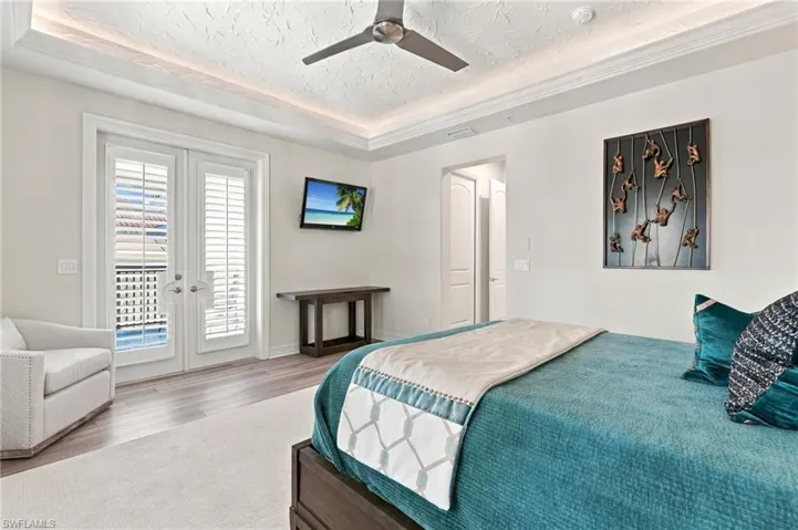 Tray ceiling with recessed lighting, ceiling fan, wood-finish flooring, and white French doors with integrated shutters