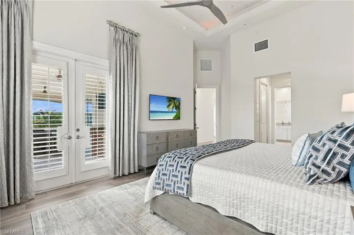 High ceilings featuring recessed tray detailing, dual French doors with plantation shutters, and wood-finish flooring