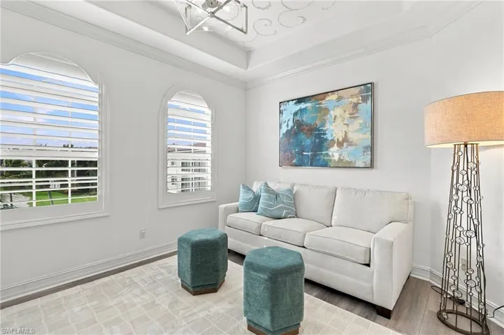 Tray ceiling with crown molding, dual arched windows with plantation shutters, geometric chandelier, and wood-finish flooring